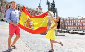 A couple holding a Spanish flag in front of a statue, representing their admiration for Spain and their eagerness to learn conversational Spanish