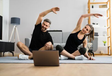 a couple practicing yoga poses in front of a laptop during a 15-minute morning workout session