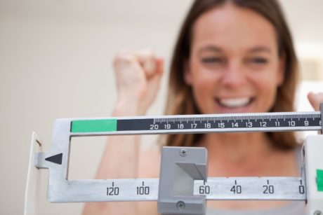 a woman holds a weight scale, symbolizing her journey in a weight loss course