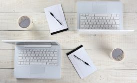 three laptops and a cup of coffee arranged on a wooden table, showcasing a workspace setup in Adobe InDesign CC