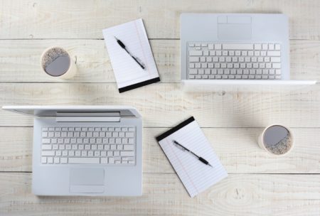 three laptops and a cup of coffee arranged on a wooden table, showcasing a workspace setup in Adobe InDesign CC