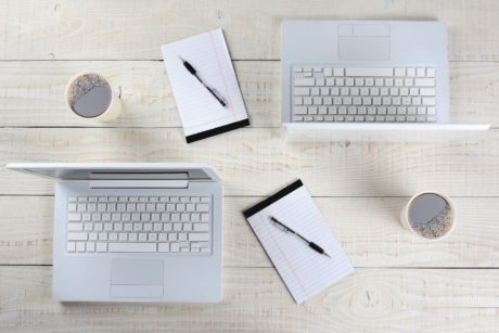 three laptops and a cup of coffee arranged on a wooden table, showcasing a workspace setup in Adobe InDesign CC