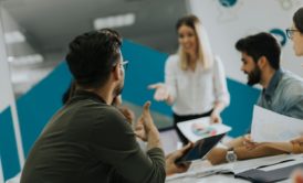 A man leading a training session on train the trainer with a group of people sitting attentively around a table