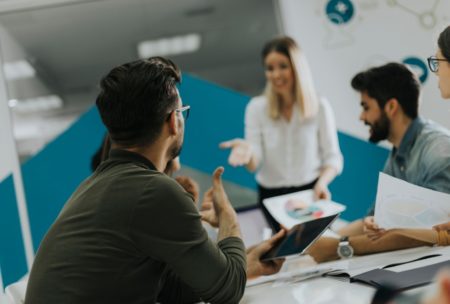 A man leading a training session on train the trainer with a group of people sitting attentively around a table