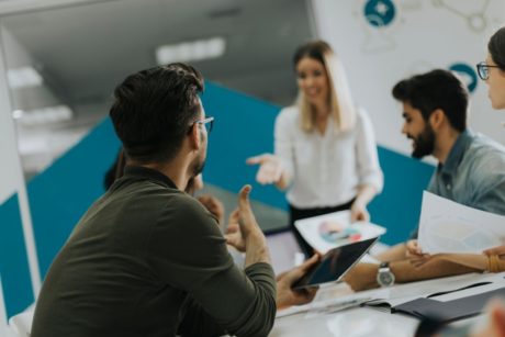 A man leading a training session on train the trainer with a group of people sitting attentively around a table