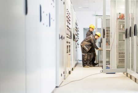 Two men working in a large room with electrical equipment in an Air Insulated Electrical Substation Design