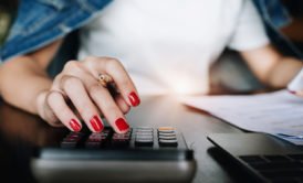 a woman with red nails calculates on a desk, focused on her swing trading course materials
