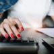 a woman with red nails calculates on a desk, focused on her swing trading course materials