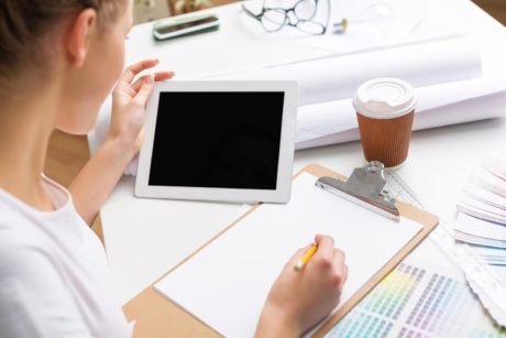 woman writing and holding tablet device