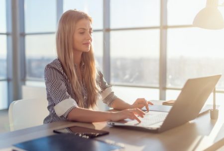 a woman sits at a desk with a laptop, engaged in an online copywriting course, focused and taking notes