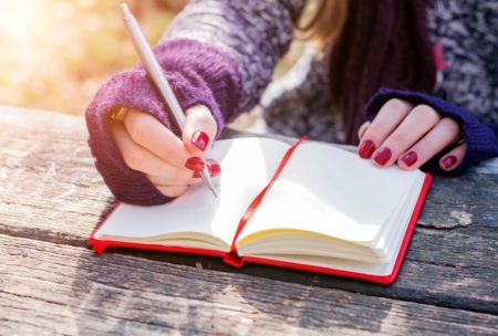 A woman diligently writes in a notebook using a pen, actively engaging in the practice of copywriting 101