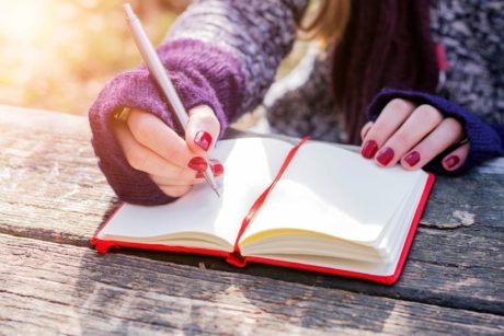 A woman diligently writes in a notebook using a pen, actively engaging in the practice of copywriting 101