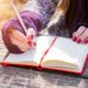 A woman diligently writes in a notebook using a pen, actively engaging in the practice of copywriting 101