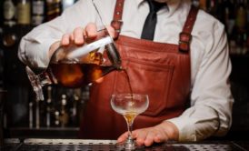 A bartender pours a drink into a glass, demonstrating bartending skills for beginners