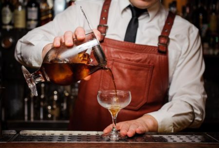 A bartender pours a drink into a glass, demonstrating bartending skills for beginners