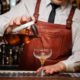 A bartender pours a drink into a glass, demonstrating bartending skills for beginners