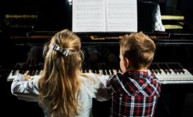 Two children immersed in piano lessons for kids, playing the piano with enthusiasm