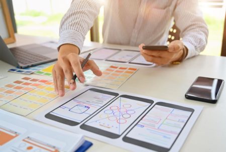 a man designing a mobile app on a smartphone and laptop, learning how to become a ux designer