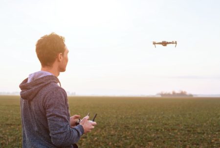 In a field, a man with beginner aerial videography skills controls a drone, capturing mesmerizing footage