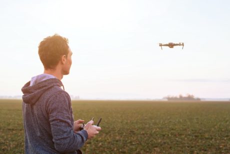 In a field, a man with beginner aerial videography skills controls a drone, capturing mesmerizing footage