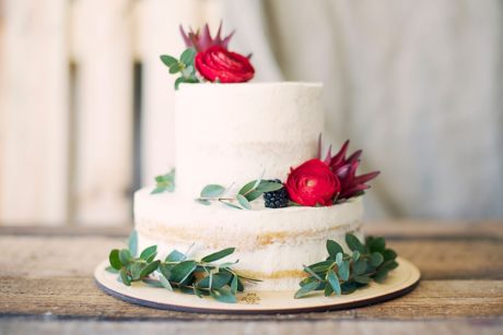 beautifully decorated wedding cake adorned with red roses and leaves, showcasing skills from a cake decorating course