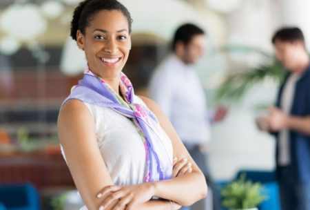 a poised woman in a business office, with coworkers in the background, highlighting the theme of confidence coaching for women