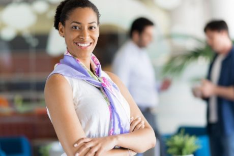 a poised woman in a business office, with coworkers in the background, highlighting the theme of confidence coaching for women