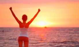 woman raising arms looking at sunset