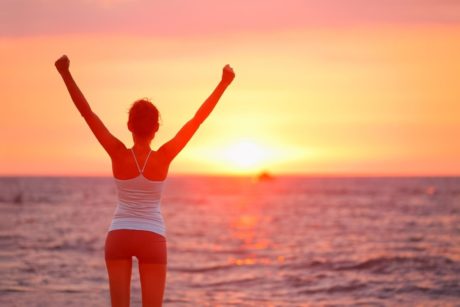 woman raising arms looking at sunset