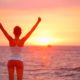 woman raising arms looking at sunset