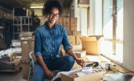 a woman in a warehouse surrounded by boxes, working on a laptop for her eBay dropshipping business