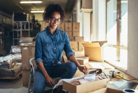 a woman in a warehouse surrounded by boxes, working on a laptop for her eBay dropshipping business