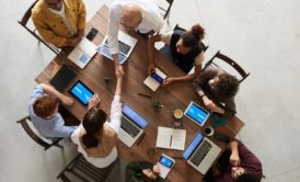 a diverse group of individuals collaborates around a table, laptops open, guided by an emotionally intelligent leader