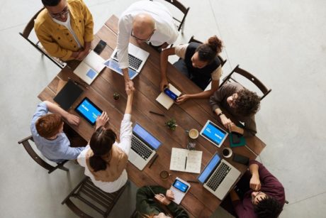 a diverse group of individuals collaborates around a table, laptops open, guided by an emotionally intelligent leader