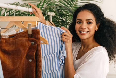 A woman happily holding a shirt on a rack, showcasing trendy fashion styles for ladies