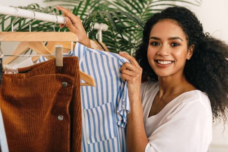 A woman happily holding a shirt on a rack, showcasing trendy fashion styles for ladies