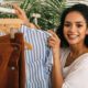 A woman happily holding a shirt on a rack, showcasing trendy fashion styles for ladies