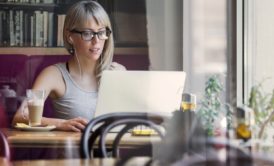 A woman in glasses working on a laptop at a table, focusing on freelance strategy consulting