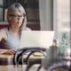 A woman in glasses working on a laptop at a table, focusing on freelance strategy consulting