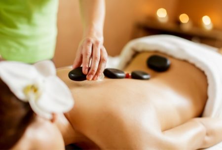 a woman lying face down on a massage table receiving a hot stones massage therapy