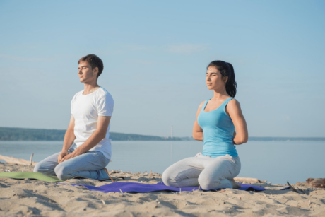 A serene couple practicing yoga on a sandy beach during a mindfulness meditation course