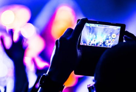 Concertgoer records lively stage performance with vibrant lighting and dynamic musicians during a video and audio production event using their smartphone