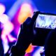 Concertgoer records lively stage performance with vibrant lighting and dynamic musicians during a video and audio production event using their smartphone