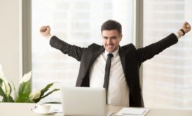 A triumphant man in a suit raises his arms at his desk, symbolizing Motivation Mastery