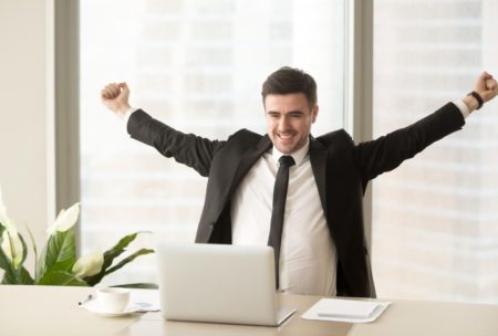 A triumphant man in a suit raises his arms at his desk, symbolizing Motivation Mastery