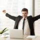 A triumphant man in a suit raises his arms at his desk, symbolizing Motivation Mastery