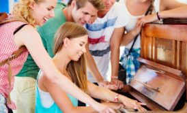 A group of young people having fun playing an old piano, learning easy popular songs to play on piano for beginners