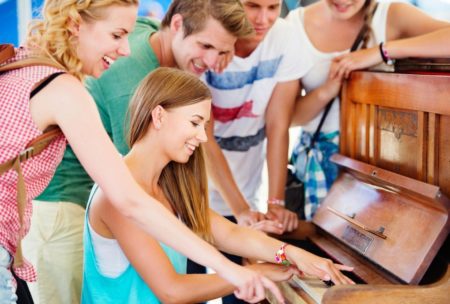 A group of young people having fun playing an old piano, learning easy popular songs to play on piano for beginners