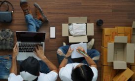 two people on the floor with laptops and boxes, collaborating on an Amazon FBA product launch strategy