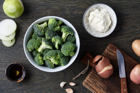 A raw food recipe featuring broccoli, onions, and various ingredients on a wooden table.
